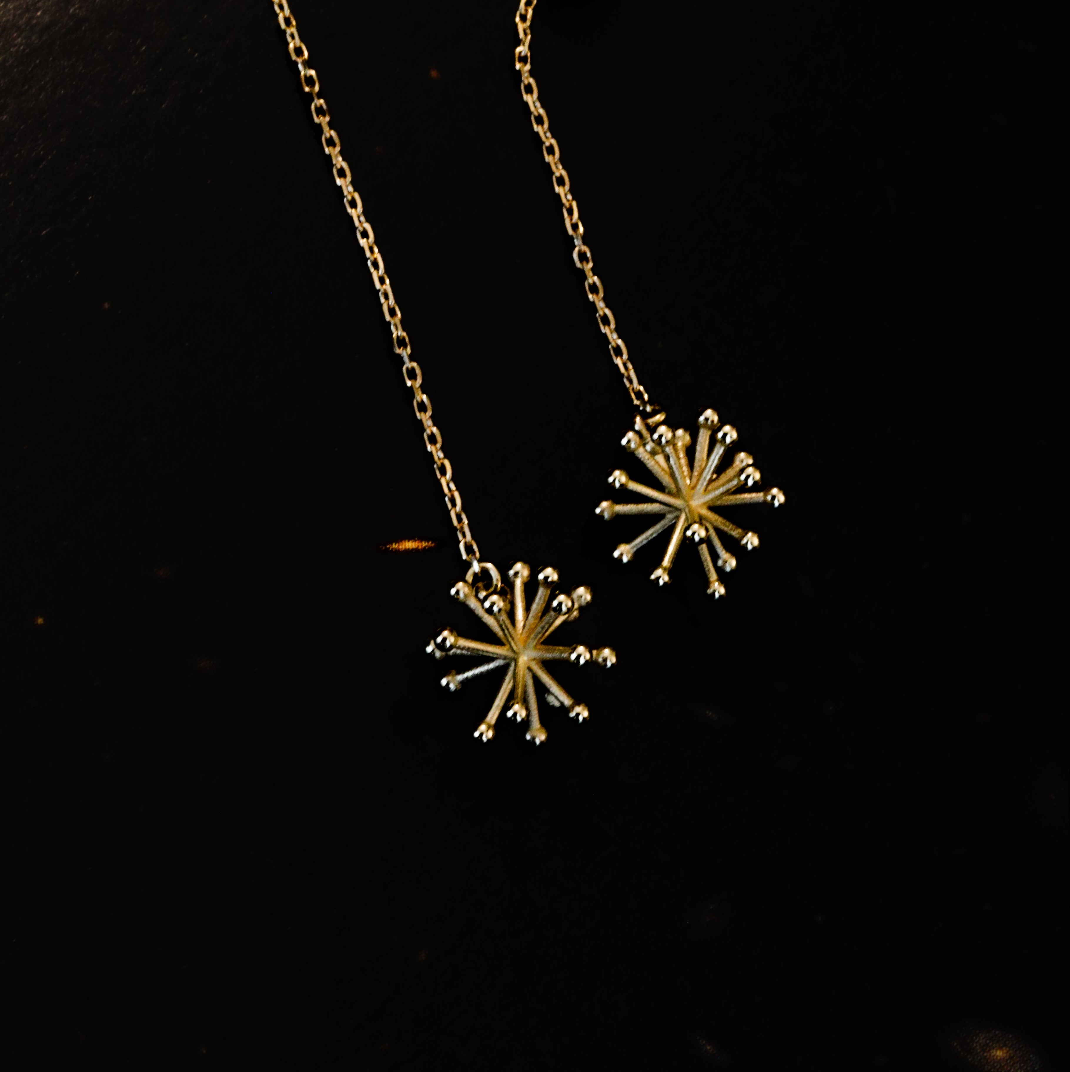 A pair of gold dangle earrings with starburst-shaped pendants, shown on a dark, reflective surface.